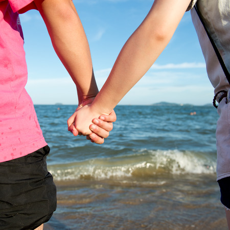Summer couple holding hands in front of the sea.の写真素材