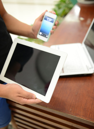 phone and tablet pc in hand and laptop on the table.の写真素材