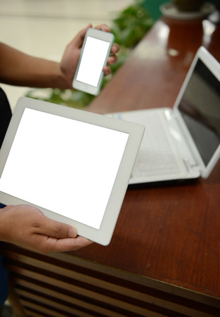 phone and tablet pc in hand and laptop on the table.の写真素材