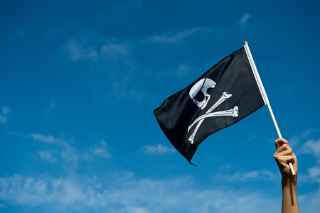 skull flag in hand waving on blue sky background.の写真素材