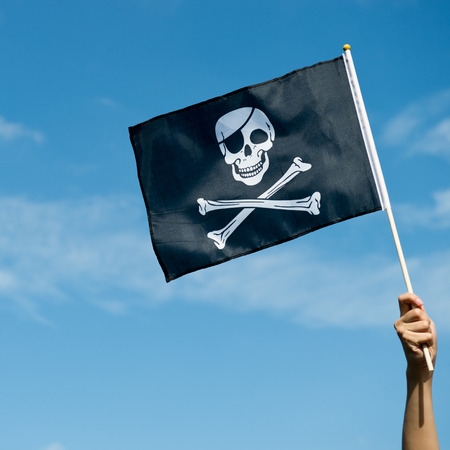 skull flag in hand waving on blue sky background.の写真素材