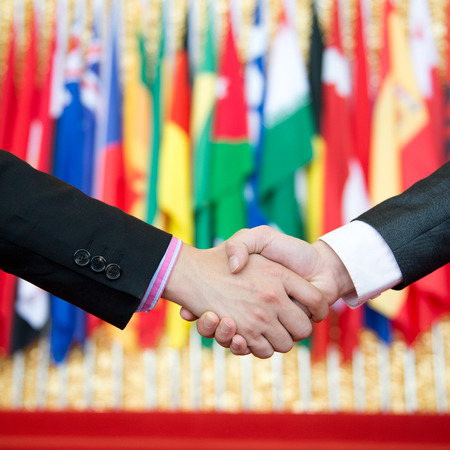 Businessmen shaking hands in front of the multi - national flag.    international businessの写真素材