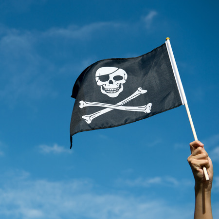 skull flag in hand waving on blue sky background.の写真素材