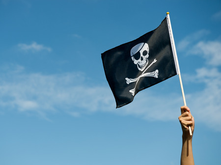 skull flag in hand waving on blue sky background.の写真素材