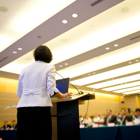 Business woman is making a speech in front of a big audience at a conference hall.の写真素材
