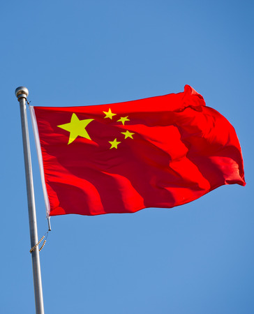 Chinese flag with flag pole waving in the wind over blue sky background.の写真素材