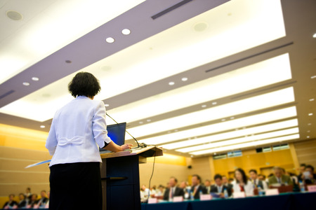 Business woman is making a speech in front of a big audience at a conference hall.の写真素材