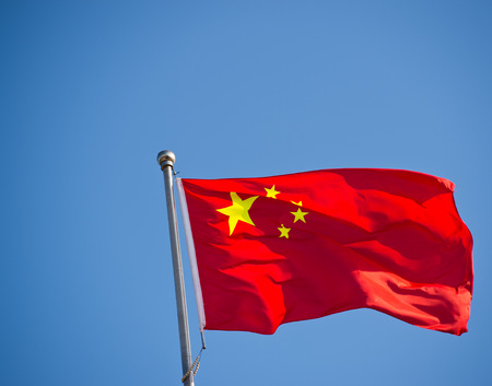 Chinese flag with flag pole waving in the wind over blue sky background.の写真素材