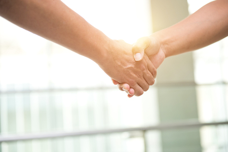 Two men shaking hands in a modern office building.の写真素材