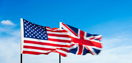 USA and Britain flags against blue sky backgroundの写真素材