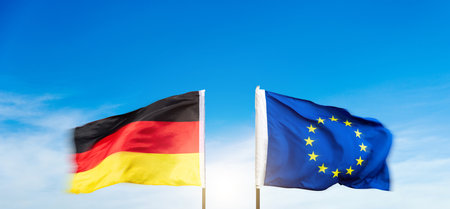 German and European Union flags against blue sky backgroundの写真素材
