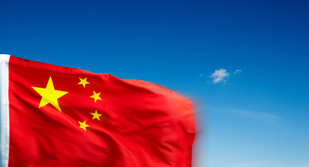 Chinese flag on pole waving in the wind against blue skyの写真素材