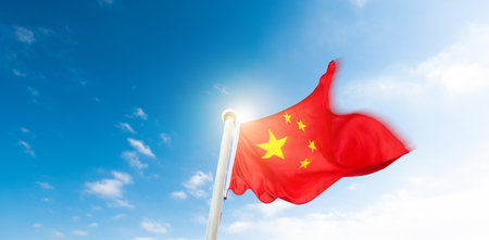 Chinese flag on pole waving in the wind against blue skyの写真素材