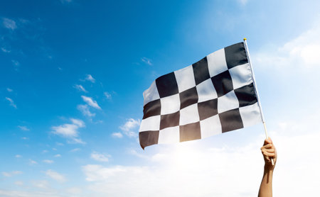Checkered race flag in hand against blue skyの写真素材