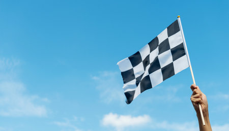 Checkered race flag in hand against blue skyの写真素材