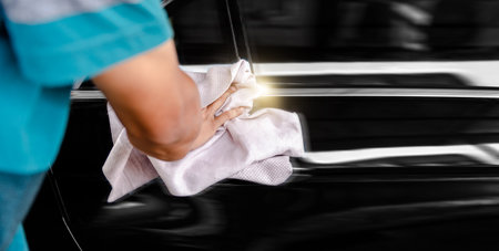 Car service worker cleaning and polishing black car with a ragの写真素材