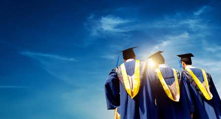 Rear view of three graduates standing in a line against blue skyの写真素材