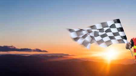 Checkered race flag in hand against sunset skyの写真素材