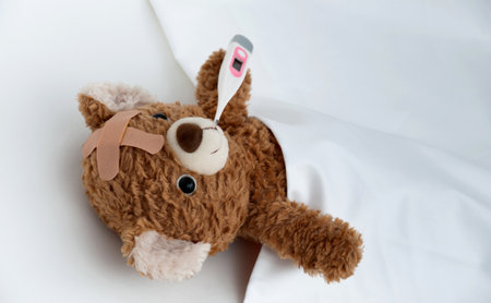 Teddy bear ill in bed with thermometerの写真素材