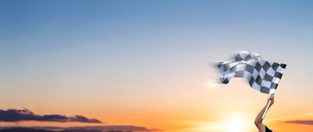 Checkered race flag in hand against sunset skyの写真素材