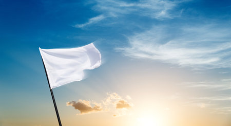 White flag flying against sunset sky backgroundの写真素材