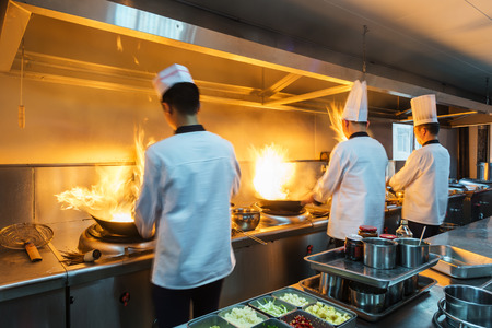 Chef in restaurant kitchen at stove with pan, doing flambe on foodの写真素材