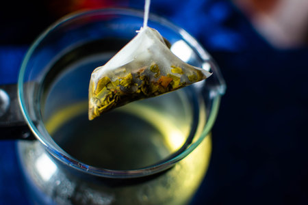 a teabag and a glass jar filled with tea. teabag has just been taken out of the jar. background is...