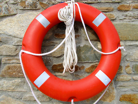 Orange and white lifebuoy ring with a stone wall in backgroundの写真素材