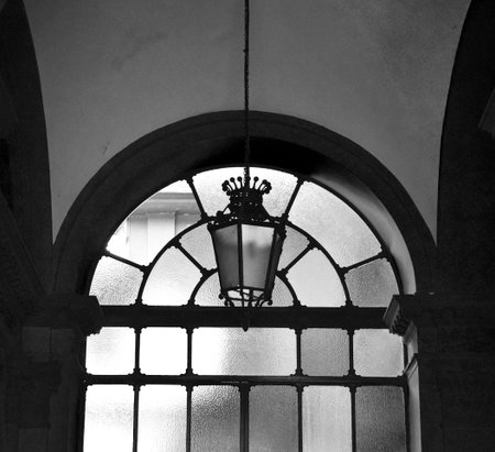 An ancient stained glass window with a lantern in an old building. Black and white.