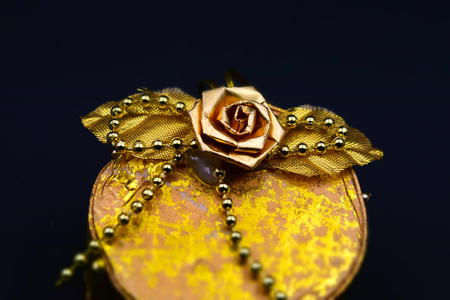 A handmade little golden box with beads, leaves and a rose. Black background. Tilt-shift effect applied.の写真素材
