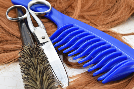 Concept for hairdresser: scissors, blue comb, brush and a lock of copper hair.の写真素材