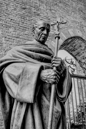An ancient statue of an old saint with a cross near an Italian church. HDR effect and black and white.のeditorial素材