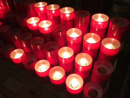 Many electrical plastic red votive candles in a dark church on black background.の写真素材