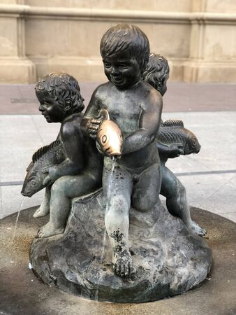 A fountain with a dark stone statue of three small children or cherubsの写真素材