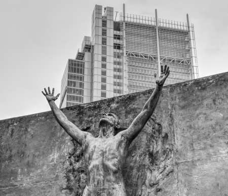 A statue of a man with arm raised and a skyscraper in the background. Black and white.のeditorial素材