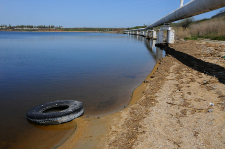 Car tires on the shore Hadzhibeysky estuary. Eutrophication of the reservoir, the problem of ecologyの写真素材