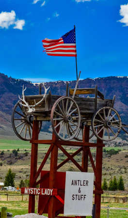USA, MONTANA - APRIL 28, 2018: Art object, vintage cart with deer antlers, American flag on a background of mountains. Montana natureのeditorial素材
