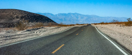 Straight asphalt road in a rocky desert in a valley towards high mountains, California