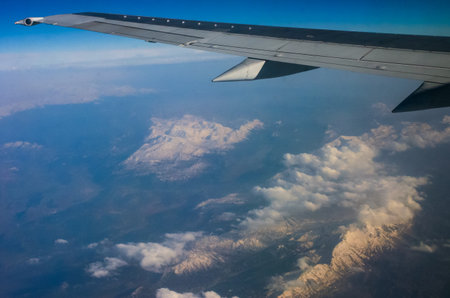Clouds and mountains below, view from an airplane windowの写真素材