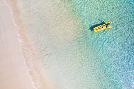 Young woman in hat relaxing on the yellow air mattress in tropical seaの写真素材