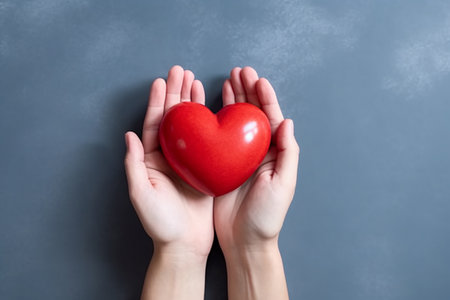Hands holding a red heart against a gray backgroundの素材