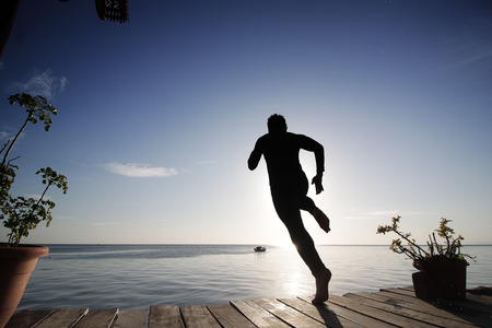 silhouette of a man jumping from a balcony to open sea waterの写真素材