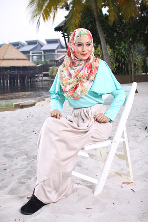 high fashion muslim woman sitting at wooden white chair with beach backgroundの写真素材