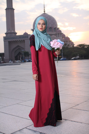high fashion muslim woman holding a flower with mosque background at sunsetの写真素材
