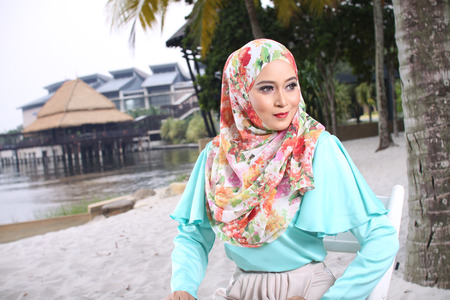 high fashion muslim woman sitting at wooden white chair with beach backgroundの写真素材