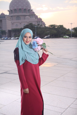 high fashion muslim women holding a flower with mosque background at sunsetの写真素材