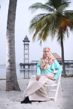 high fashion muslim women sitting at wooden white chair with beach backgroundの写真素材