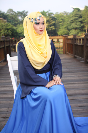 high fashion muslim woman posing and sitting at white chair with wooden backgroundの写真素材