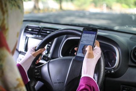 muslim woman looking at her mobile phone while driving carのeditorial素材
