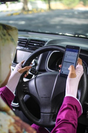 muslim woman looking at her mobile phone while driving car